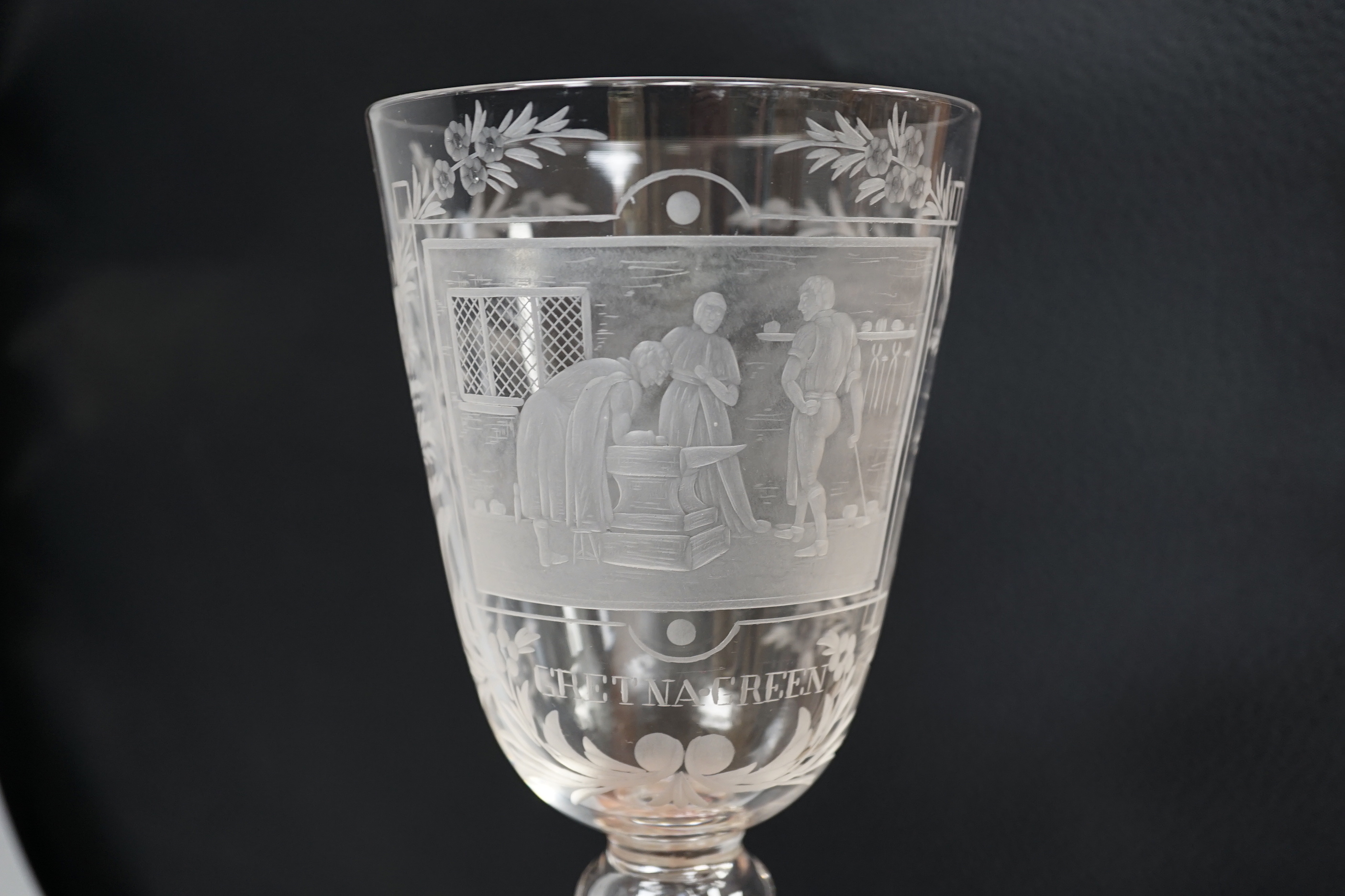 A lead crystal commemorative Gretna Green goblet, with fine engraving of a blacksmith and couple signing the register on an anvil, the panel surrounded by floral engraving, ‘GRETNA GREEN’ below, 23.9cm high